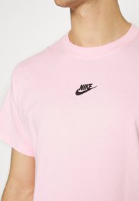 Lyserød bomuld T-shirt med rund hals og korte ærmer. Har en lille sort broderet Nike-logo på brystet.