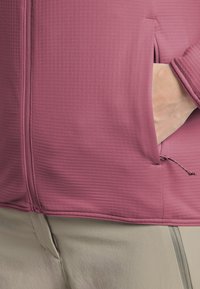 Veste rose ajustée et côtelée avec des poches zippées. L'ourlet est resserré avec des cordons réglables pour un ajustement sur mesure.