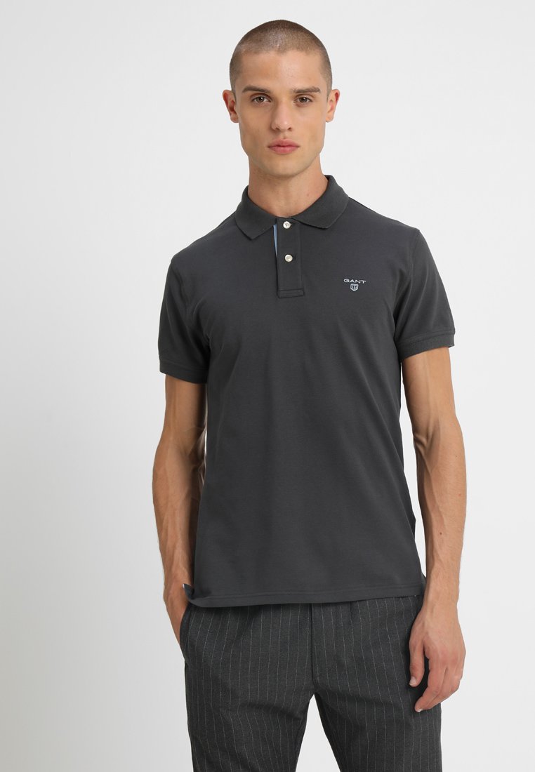 Dunkelgraues Poloshirt mit einem Zwei-Knopf-Kragen, kurzen Ärmeln und einem Logo auf der Brust, hergestellt aus einem weichen, strukturierten Baumwollmaterial.
