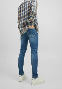 Jeans de mezclilla azul con un corte ajustado, combinados con una camisa de franela de cuadros; cuenta con un bolsillo trasero y zapatillas blancas.