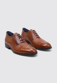 Chaussures en cuir brun avec une texture lisse, bouts pointus et un design à laçage à cinq œillets. Caractéristiques d'une doublure bleue contrastée et d'un talon carré.
