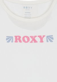Bílý organický bavlněný tričko s motivem "ROXY" v růžových a modrých blokových písmenech s akcenty šipky, s kulatým výstřihem a krátkými rukávy.