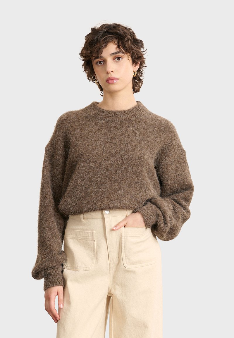 Maglione knit marrone, fluffy, con collo rotondo e maniche lunghe e voluminose, abbinato a pantaloni beige chiaro a vita alta.