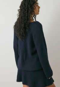 Donkerblauwe gebreide trui met een textuurafwerking, met een losse pasvorm en lange mouwen, gecombineerd met een bijpassende rok.