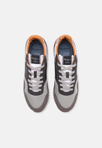 Sneakers with a grey, black, and white color scheme. Features leather and textile materials, round toe, white laces, and contrasting orange lining.