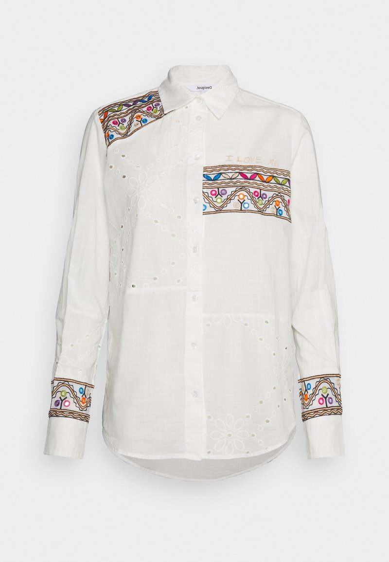 Chemise blanche à manches longues boutonnée avec des motifs brodés colorés sur l'épaule, la poche poitrine et les poignets, et des détails subtils en œillets floraux.