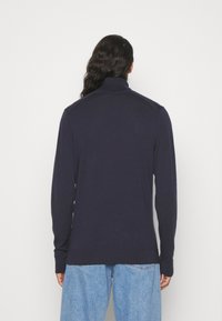 Dunkelblauer Strickpullover mit hohem Kragen, langen Ärmeln und gerippten Bündchen und Saum. Hat eine glatte Textur und dezente Schulterakzente.