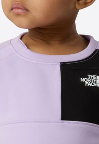 Violetti collegepaita, jossa musta paneeli ja "The North Face" -logo; pehmeää kangasta, pyöreä pääntie, kontrastiväriset palat ja ompelukoristukset.