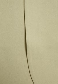 Gros plan sur un tissu beige à tissage fin, présentant une couture verticale centrale créant un pli subtil.