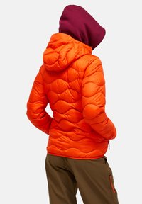 Orangene Pufferjacke mit gesteppter Textur und Kapuze, kombiniert mit braunen Hosen. Merkmale sind eine Reißverschlusstasche und elastische Bündchen.