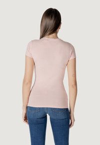 Camiseta ajustada de color rosa claro con mangas cortas, cuello redondo y tela suave, combinada con jeans azul oscuro con bolsillos traseros.