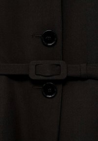 Gros plan sur un tissu noir avec deux boutons noirs et une ceinture en tissu assorti avec une boucle rectangulaire.