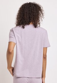 Camiseta de manga corta en un suave color púrpura claro, fabricada con un tejido suave, con un corte recto y detalles de costura mínimos en el escote y el dobladillo.