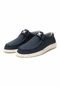 Zapatos sin cordones de color azul marino con un upper de tela texturizada, suela blanca con manchas y un interior a rayas. Presenta un logotipo blanco en contraste en la parte delantera.