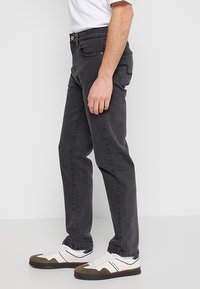 Czarne jeansy z denimu o prostym kroju, z pięcioma kieszeniami i subtelnymi detalami przeszyć. Połączone z białymi i brązowymi sneakersami.