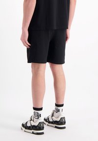 Zwarte sportshorts met een gladde textuur, gecombineerd met zwart-witte sneakers met een logo. Eenvoudig ontwerp zonder zichtbare patronen.