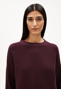 Burgunderfarbener Pullover aus strukturiertem Strick mit weitem Ausschnitt und langen Ärmeln, der einen lockeren Schnitt und subtile Nähdetails aufweist.