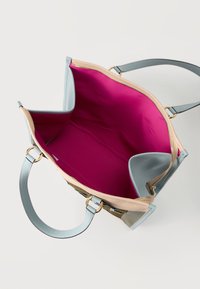 Άνω όψη ανοιχτής τσάντας χειρός από δέρμα σε μπεζ και μπλε χρώμα με έντονη ροζ υφασμάτινη επένδυση και λουριά ώμου σε απλό φόντο.