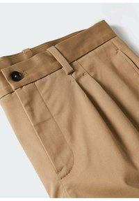 Pantalon beige avec bouton devant, passants de ceinture et poches latérales, montrant la texture du tissu et les détails de couture sur un fond clair.