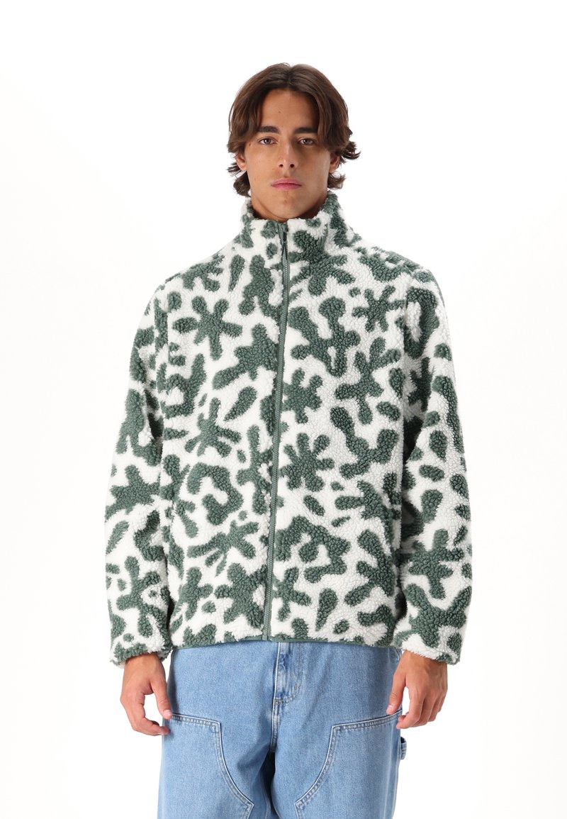 Veste en polaire avec un motif abstrait vert sur fond blanc, dotée d'un col haut et d'une fermeture éclair.
