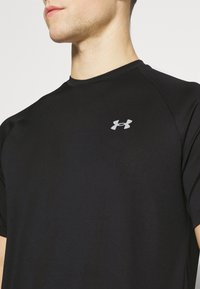 Svart, kortärmad träningsskjorta gjord av fukttransporterande material. Har en liten silverlogotyp på bröstet och rund halsringning.