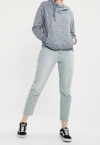 Felpa grigia con macchie multicolori, tasca a marsupio, abbinata a jeans chiari con risvolto e sneakers nere. Design semplice, stile casual.