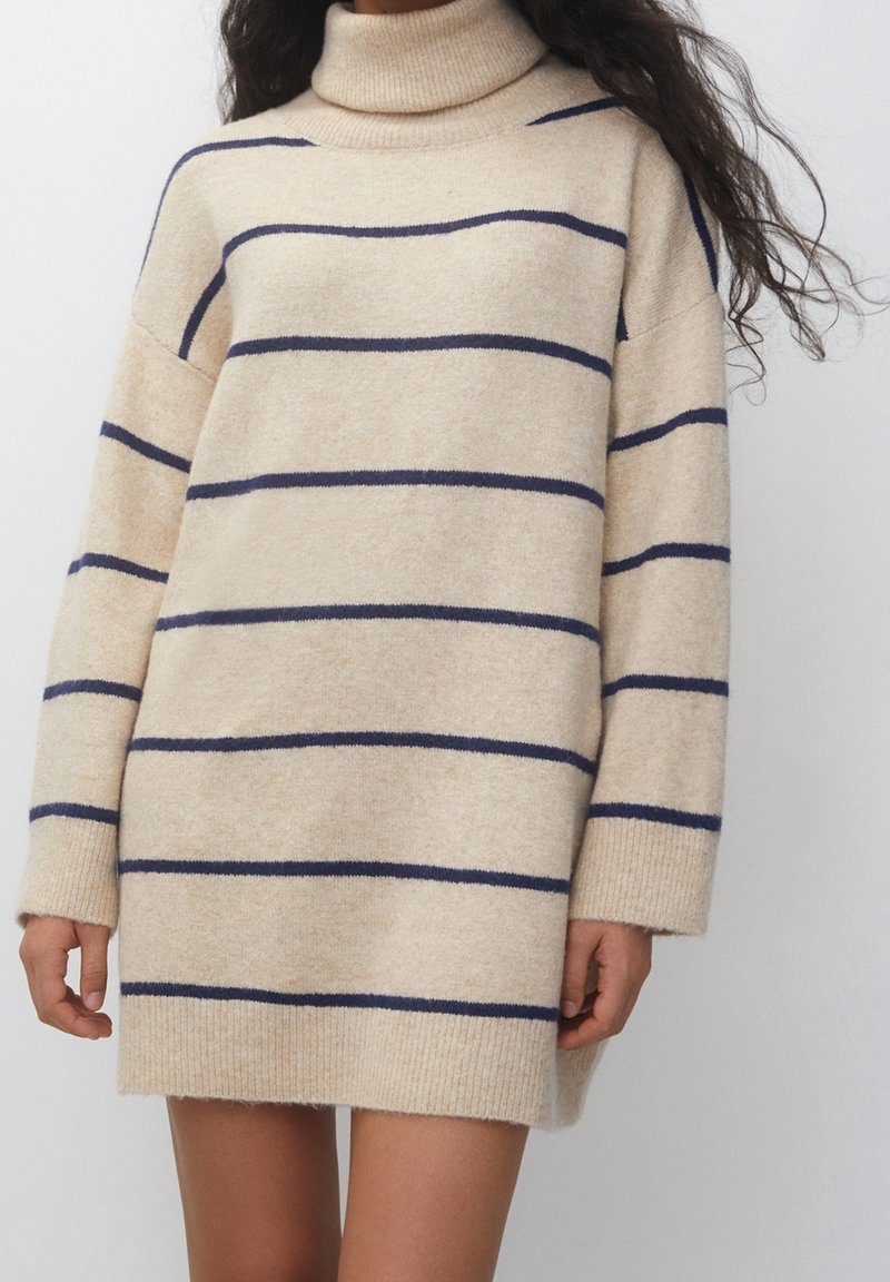 Robe-pull col roulé beige à rayures horizontales bleu marine, manches longues, poignets et ourlet côtelés portée par une personne debout.