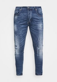 Jeans de denim azul oscuro, ajustados, con un lavado desgastado, áreas desgastadas y sutiles manchas de pintura. Presenta cinco bolsillos y un cierre de botón.