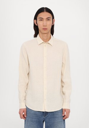 Kremfarget langermet skjorte laget av lett stoff med knappestolpe foran, spiss krage og subtil tekstur. Brukt med blå jeans.