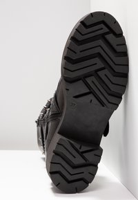 Czarny skórzany but z teksturowaną gumową podeszwą, z charakterystycznym bieżnikiem w zygzak i metalowymi ćwiekami po bokach cholewki. Rozmiar 37 oznaczony na podeszwie.