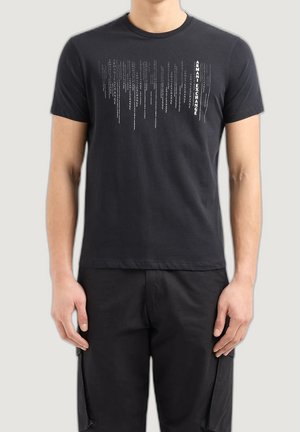 T-shirt en coton noir avec un motif de texte vertical blanc. Manches courtes, col rond et coupe régulière. Porté avec un pantalon noir assorti.