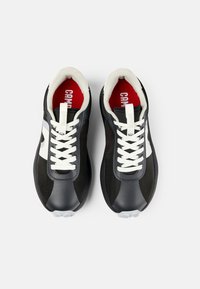 Scarpe sportive nere con accenti bianchi, dotate di una tomaia testurizzata, lacci tondi e un interno rosso con marchio visibile.
