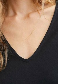 Top negro con escote en V, confeccionado en una tela suave y elástica que se ajusta al cuerpo. El escote es profundo y está definido de manera precisa, creando una estética limpia.