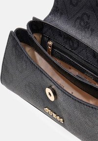 Portefeuille en cuir noir texturé partiellement ouvert montrant une doublure en tissu beige, une poche intérieure zippée et une fermeture à bouton-pression dorée avec le logo de la marque.