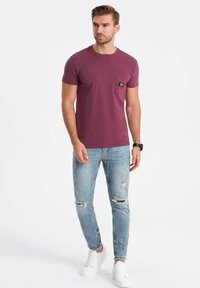 Maron t-shirt med brystlomme, parret med lyseblå slidte jeans og hvide sneakers. Slim fit og korte ærmer.