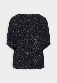 Sort bluse med hvidt lille blomsterprint, trekvart pufærmer og løs pasform, vist bagfra på en ensfarvet baggrund.