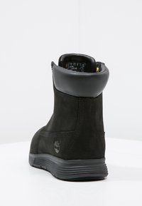 Stivaletto alla caviglia in suede nero con forma rotonda, colletto in pelle, interno imbottito e suola in gomma. Presenta un logo in rilievo sul lato.