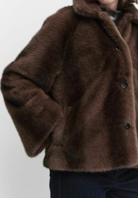 Brązowa kurtka z sztucznego futra z szerokim kołnierzem, dużymi guzikami i szerokimi rękawami. Tekstura wydaje się miękka i puchata, co tworzy przytulny wygląd.