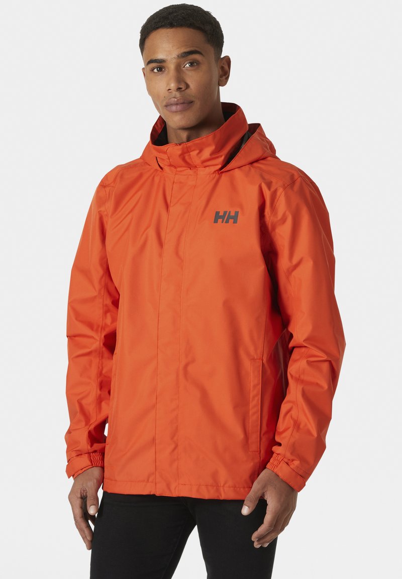 Chaqueta impermeable de un brillante color naranja, con capucha, cierre de cremallera y puños elásticos. Incluye un logotipo negro en el pecho y bolsillos laterales.