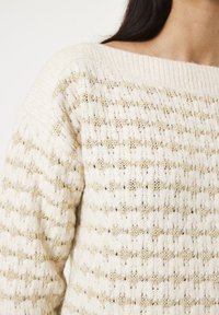 Off-shoulder gebreide trui in crème met gouden accentstrepen, voorzien van een textuurpatroon en een geribbelde halslijn.