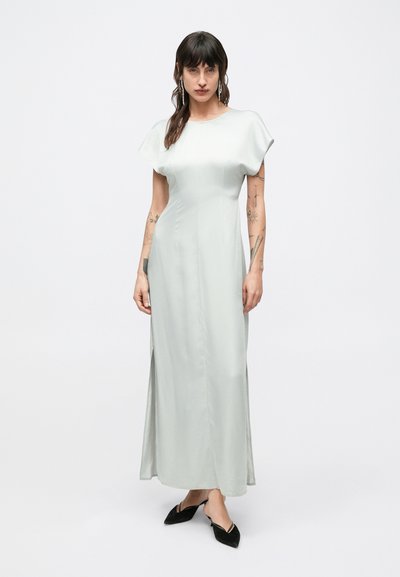 Svetlosivé maxi šaty s krátkymi, voľne padajúcimi rukávmi, bočnými rozparkami a hladkým, lesklým povrchom. Nosené s čiernymi špicatými balerínkami.