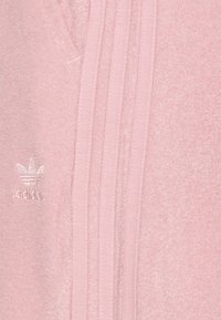 Sudadera de forro polar rosa con diseño de tres rayas, tejido texturizado y logo en relieve en el lado izquierdo. Ajuste suave y casual.