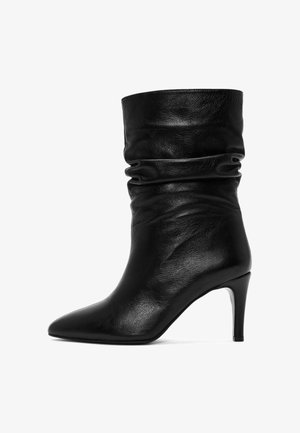 Bottine noire en cuir avec un tige ample, bout pointu et un talon haut fin. Texture lisse sans motifs ni accents visibles.