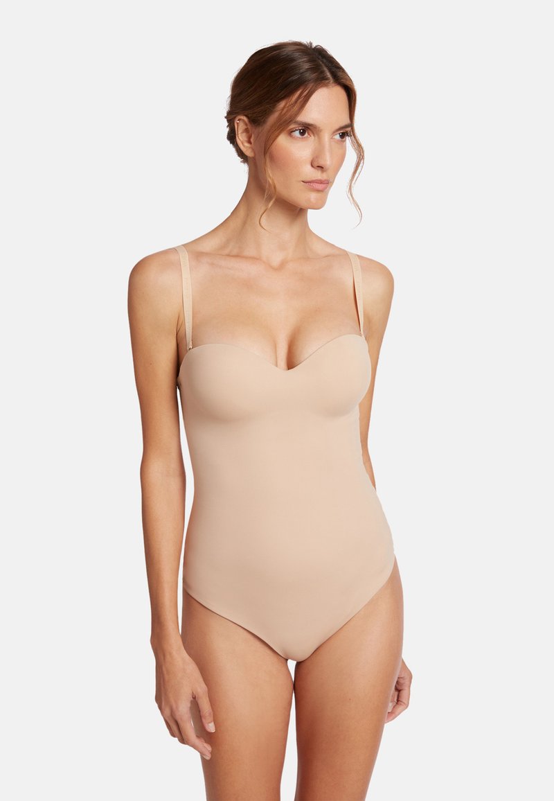 Nude bodysuit met gevormde cups, verstelbare bandjes en een gladde textuur. Heeft een diepe halslijn en een naadloos ontwerp, ideaal voor het lagen óf combineren.