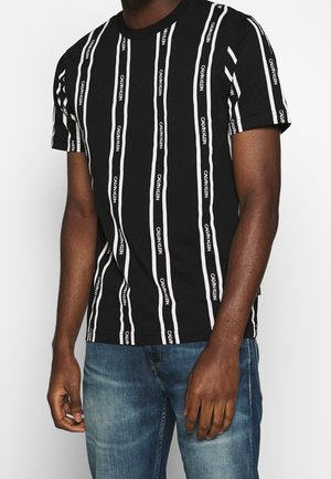 Černé bavlněné tričko s vertikálními bílými pruhy a nápisem "CALVIN KLEIN", krátkými rukávy a klasickým kulatým výstřihem.