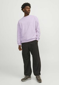 Sudadera de lavanda clara con cuello redondo y hombros caídos, combinada con pantalones negros holgados y zapatillas grises. Diseño sencillo, sin patrones.