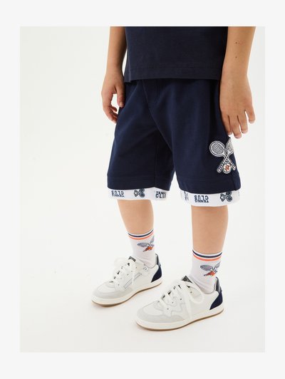 Navy shorts with tennis racket embroidery, white waistband with "Tennis Club" text. Matched with white sneakers and patterned socks.