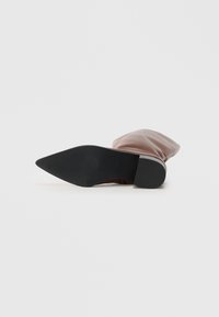 Botte slouchy rose clair avec un bout pointu et semelle en caoutchouc noire, posée à plat montrant la vue inférieure sur fond blanc.