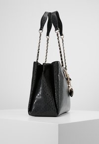 Sac fourre-tout en cuir verni noir avec motif en logo embossé, anses rehaussées de chaînes et un pendentif, doté d'une forme structurée et d'une finition brillante.