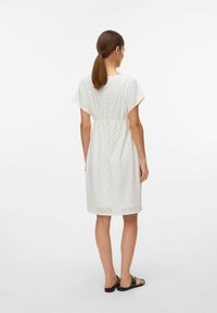 Robe en coton blanche avec un motif découpé en diamant, des manches courtes et une taille cintrée. L'ourlet présente un design décoratif découpé au laser.